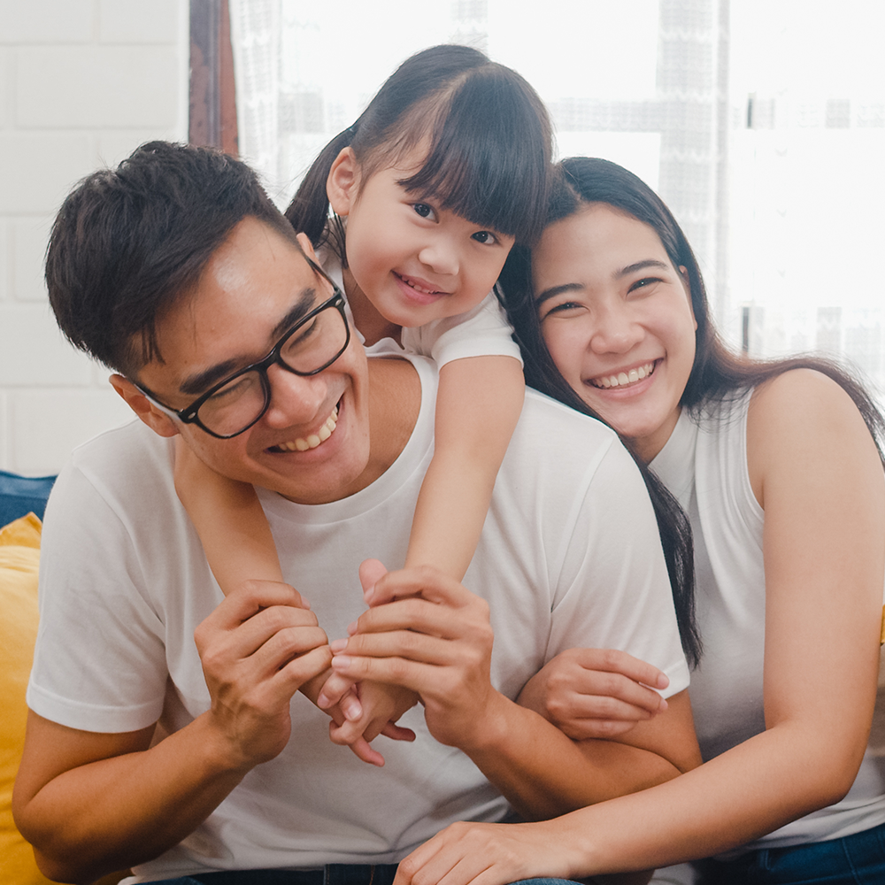 A photographic image of a young asian family including a mother, father and their daughter all embracing one another.
