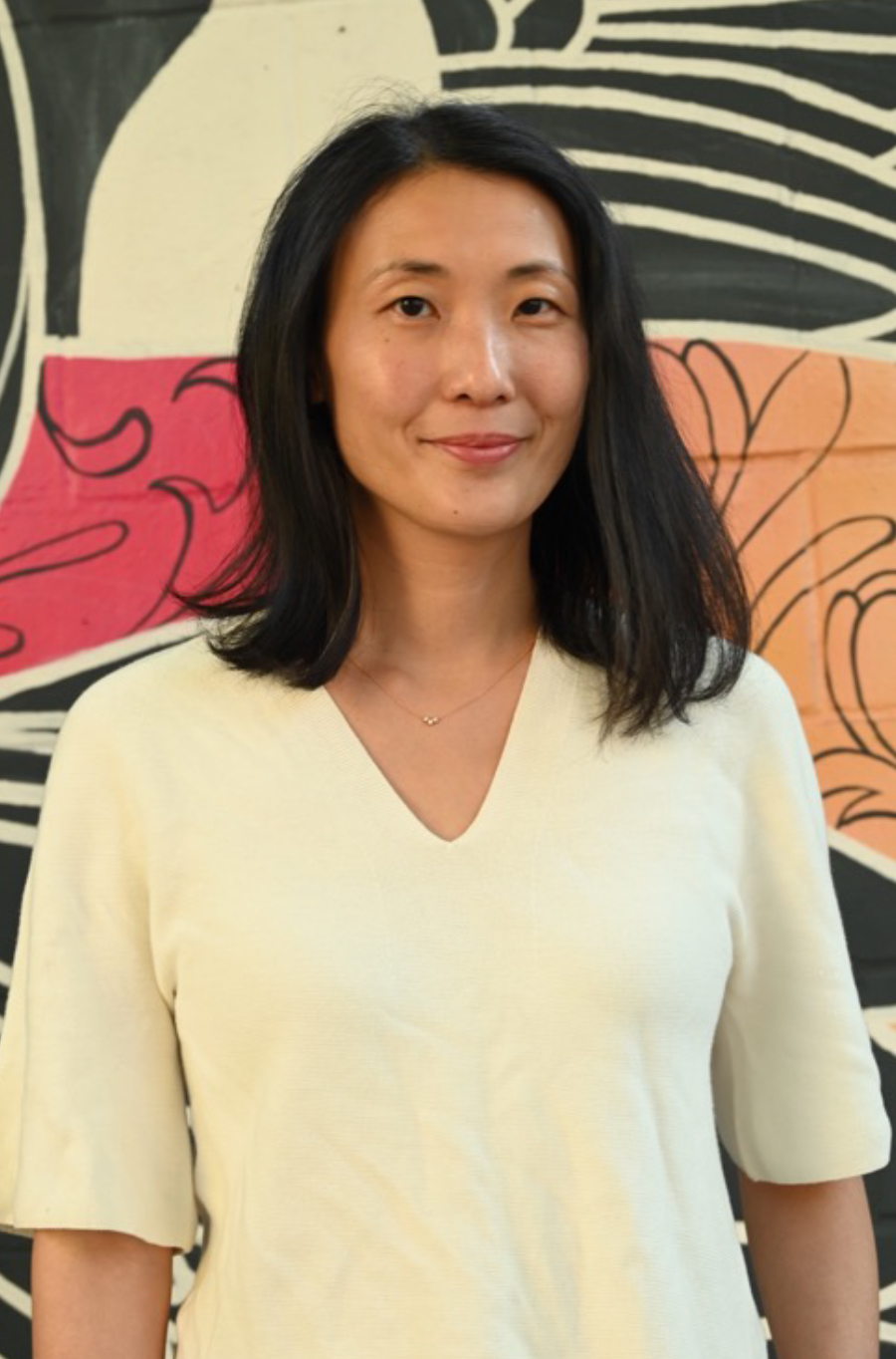 A photographic style image of Dr. Christine Ou standing against a wall with graffiti style artwork.